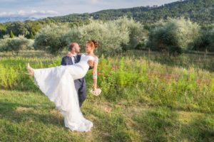 Le marié porte la mariée dans un champ de fleur et d'olivier.