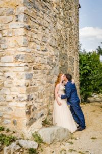 Le couple de mariés s'embrassent contre un haut mur de pierre.