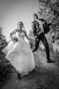 couple courant sur un chemin en habit de mariage, la mariée tient sa robe et le marié est suspendu dans les airs