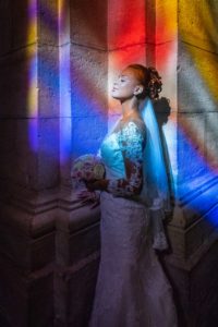 La mariée dans une église, éclairée par les tons colorés des vitraux.
