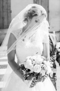 la mariée voilée regarde son bouquet de fleurs blanches avant d'entrer dans l'église
