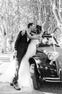 les deux mariés s'embrassent contre une voiture deux chevaux décorée pour le mariage