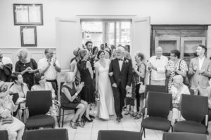 La mariée passe la porte de la salle de mariage de la mairie au bras de son père, sous les applaudissements des invités