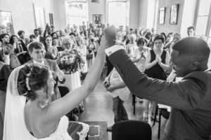 Les deux mariés dans la salle de mariage de la mairie lèvent les bras, main dans la main, face à tous leurs invités applaudissements.